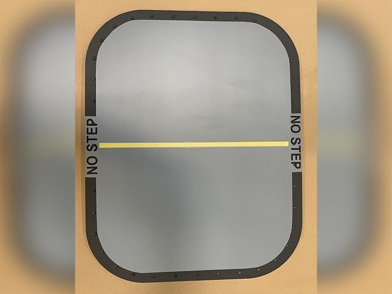 Escape hatch radome for aircraft. A rectangular panel with rounded corners painted grey. There is a dark grey border with the works "no step" on two sides and a yellow line across the center. 