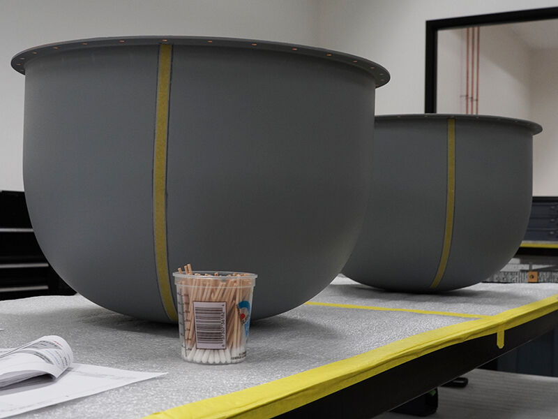 Ka-band and Ku-band radomes in assembly. Two dome shaped radomes balance upside down on an assembly table in a manufacturing environment. 