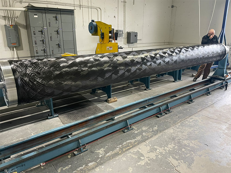 Custom filament wound carbon fiber tubular structure for an unmanned system being wound in a manufacturing facility.