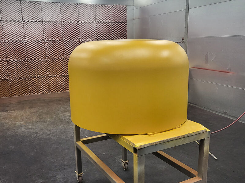 X-band belly radome in a paint booth for priming. Radome is on a table in the booth. Coating is yellow/orange.