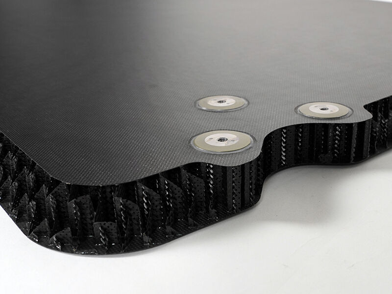 Reflector splashplate with carbon core, edge detail Detail image of a reflector splashplate with a carbon core. The carbon fiber sandwich panel has three metal inserts near the edge.