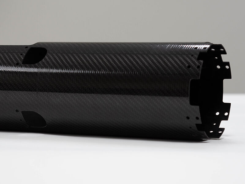 Unmanned aerial vehicle carbon fiber fuselage. Tubular structure with machined cutouts laying on a white surface on a neutral background.