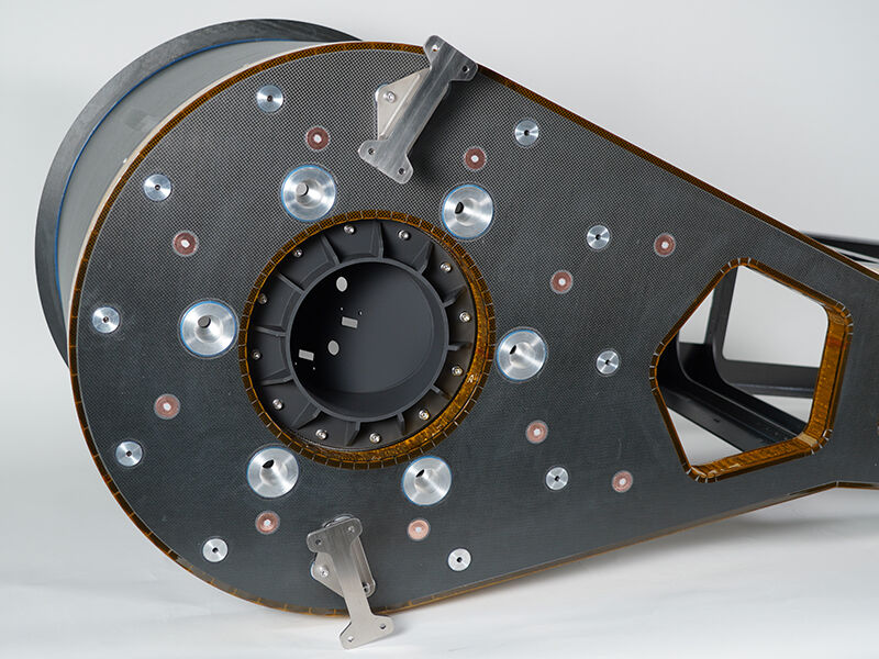 Image of the exterior underside of the EOI telescope. The bottom carbon fiber sandwich panel has multiple metallic inserts. Kapton tape wraps around the machined edges of the panel. Telescope is on a white background. 