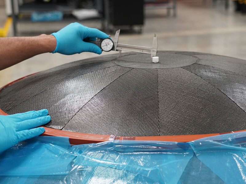 Technician measuring a carbon fiber panel during the layup of a reflector. Carbon fiber reflector under manufacture. Pausing during the layup process, the technician is measuring from the center to the edge of the center circular panel to verify accuracy.