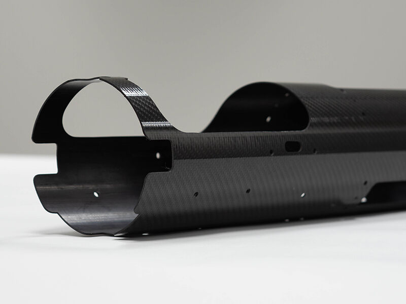 Unmanned aerial vehicle carbon fiber fuselage. Tubular structure with machined cutouts laying on a white surface on a neutral background.